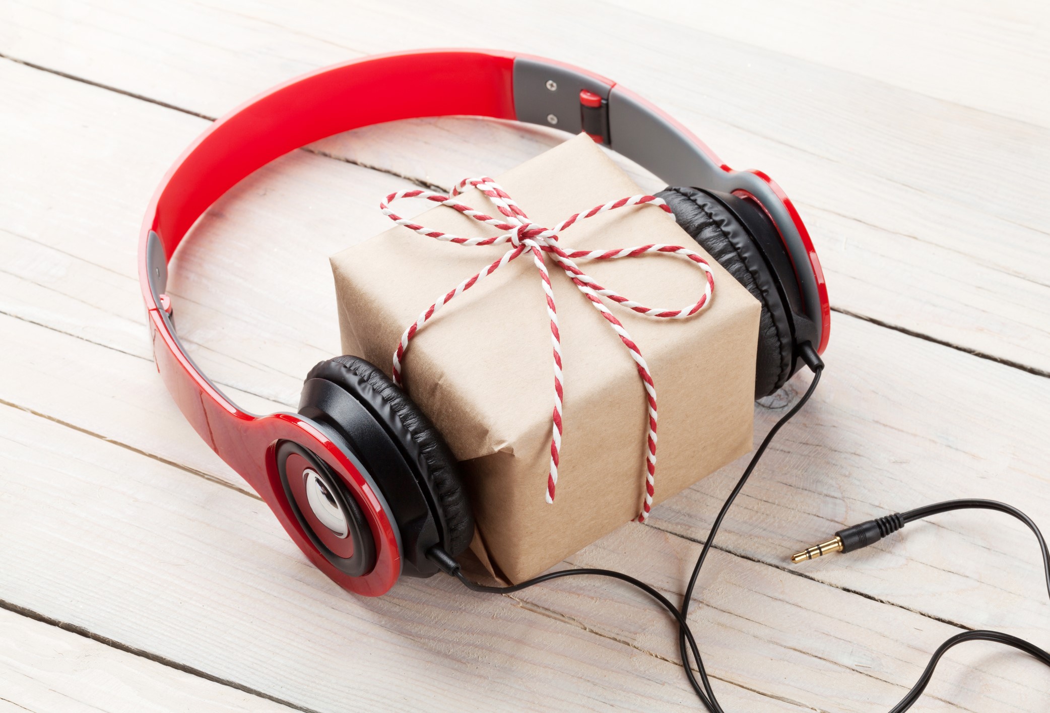 A red pair of headphones with a gift wrapped in brown paper and string